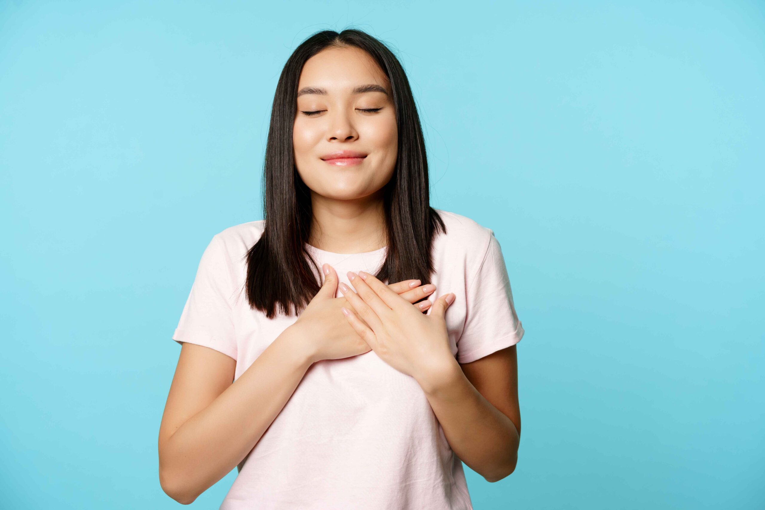 smiling-korean-woman-dreaming-holding-hands-heart-close-eyes-cherish-memory-her-soul-standing-blue-background