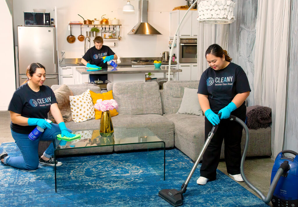 Two Cleany cleaners in uniform cleaning a bright living room and kitchen